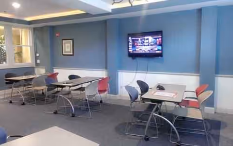 Blue-walled communal interior with tables, chairs, and a wall-mounted TV.
