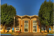 Front entrance of Metropolis Rehabilitation & Health Care Center showing the building facade with double doors, two large trees, and marked handicap parking spaces.