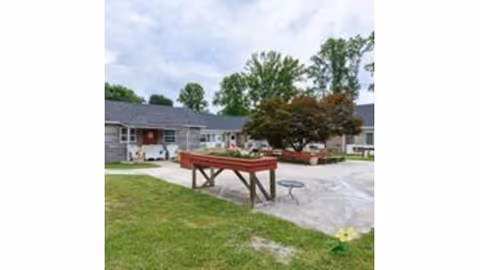 Courtyard with a raised planter and outdoor seating in front of single-story rehab center buildings and trees.