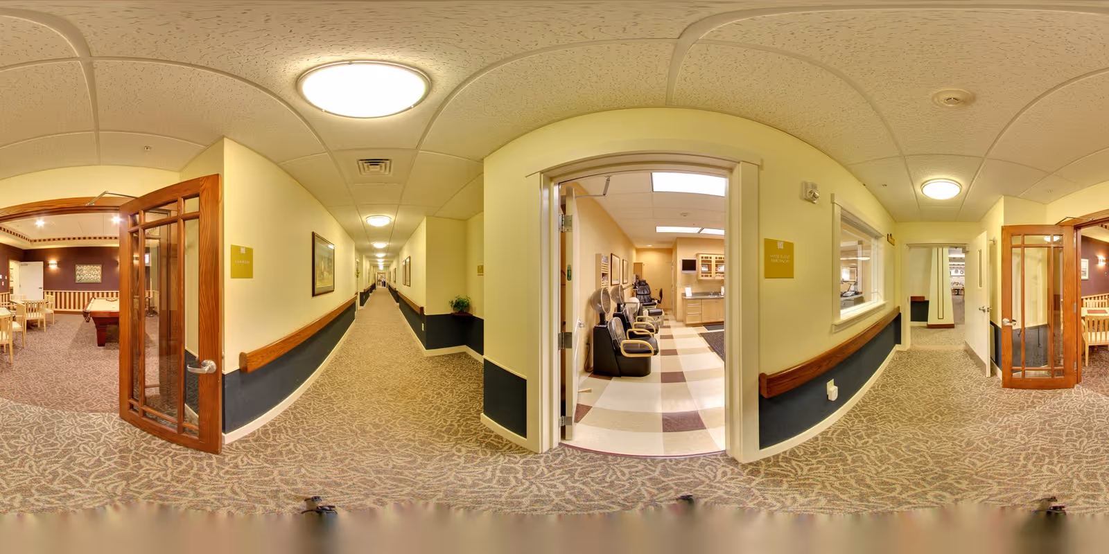 Carpeted interior corridor of a senior living facility with open doorways to a lounge and salon on either side.