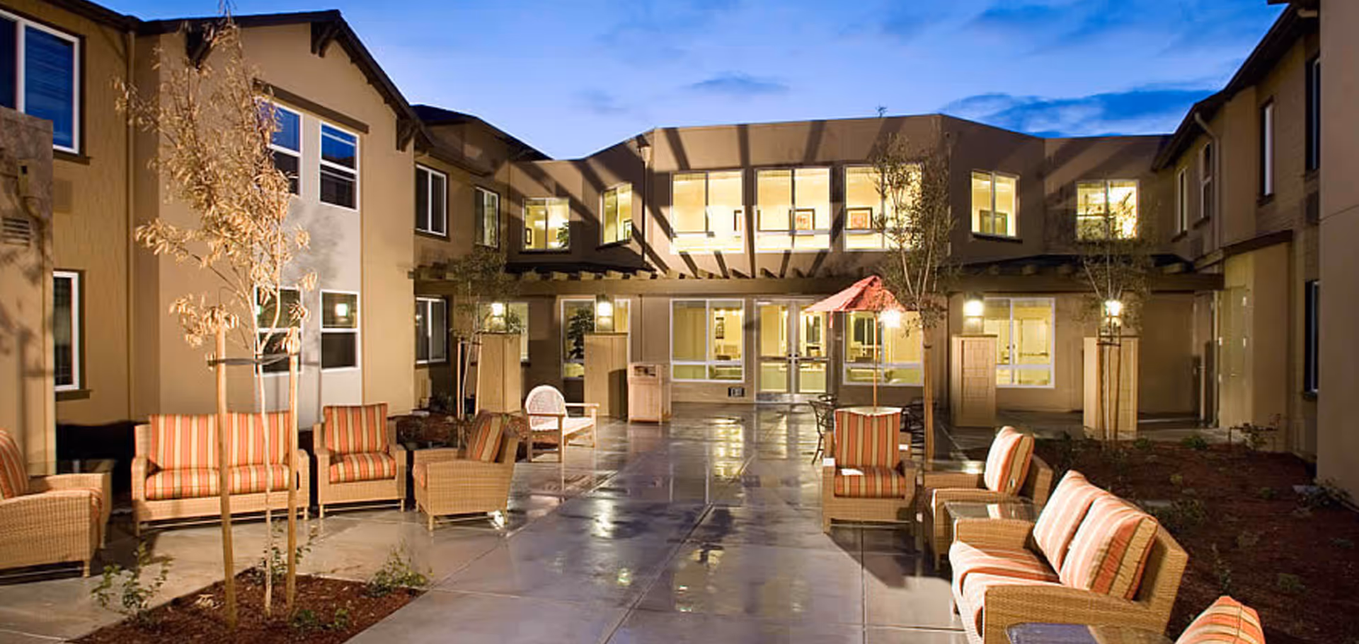 Evening courtyard of The Parkview with wicker seating and striped cushions on a paved patio in front of a two-story building.