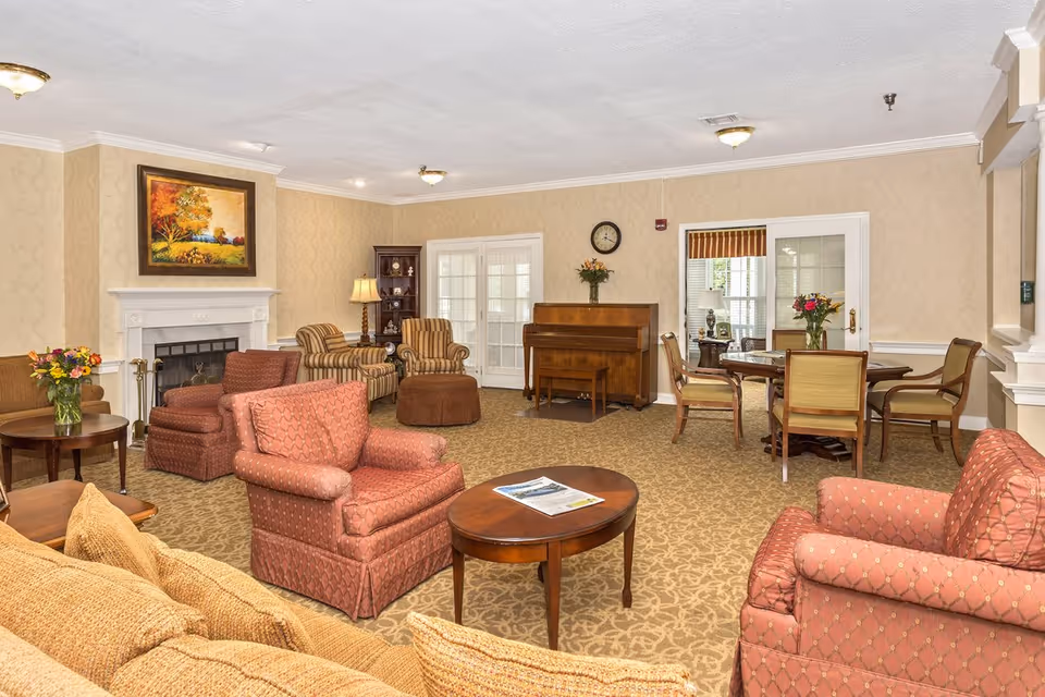 Well-appointed common lounge with upholstered chairs and sofas, coffee tables, a fireplace, a piano, and a dining/game table.