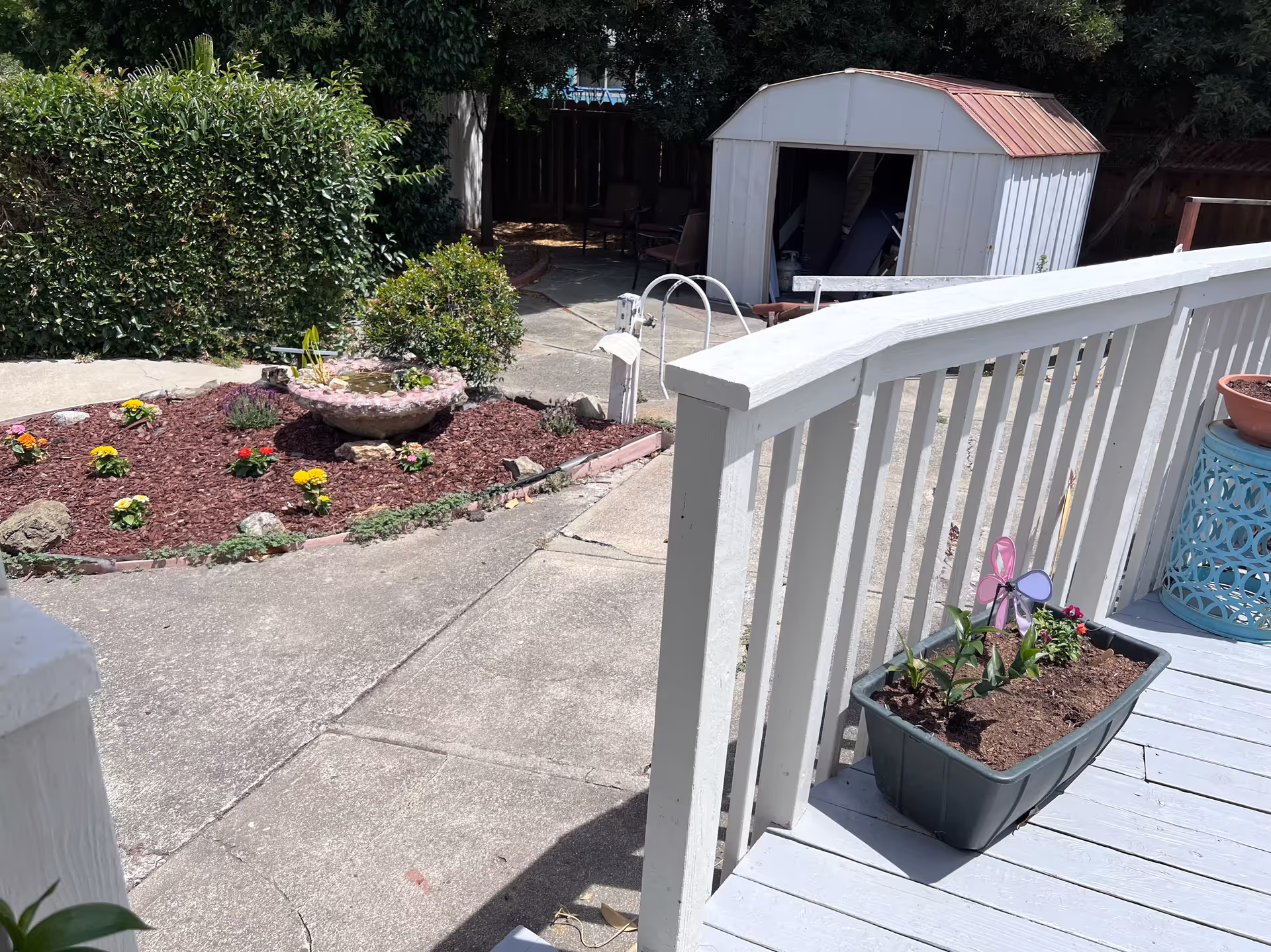White deck railing with potted plants overlooks a mulched garden and shed behind.