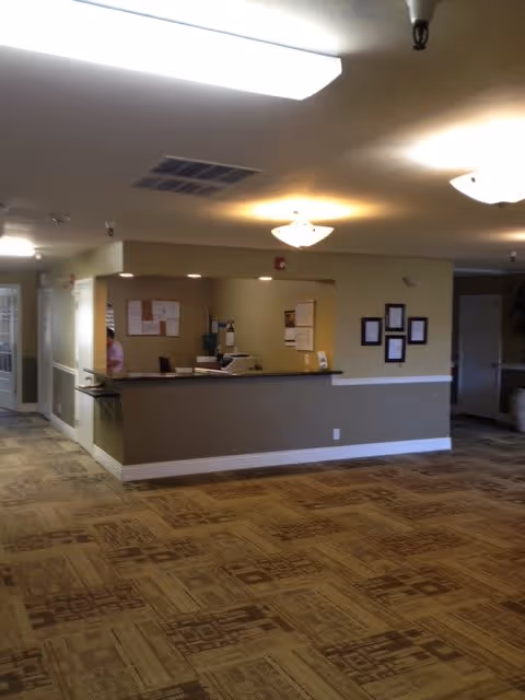 Reception desk and lobby area of a senior living facility with patterned carpet and overhead lighting.