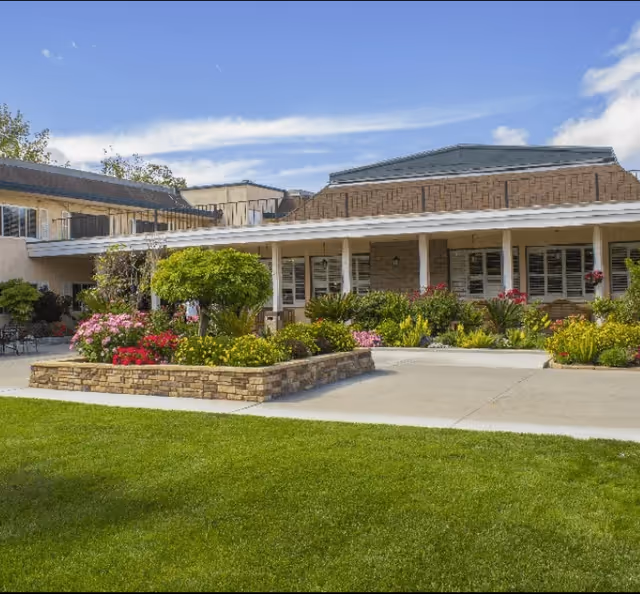 Senior living facility exterior with a landscaped entrance and lawn under a blue sky.