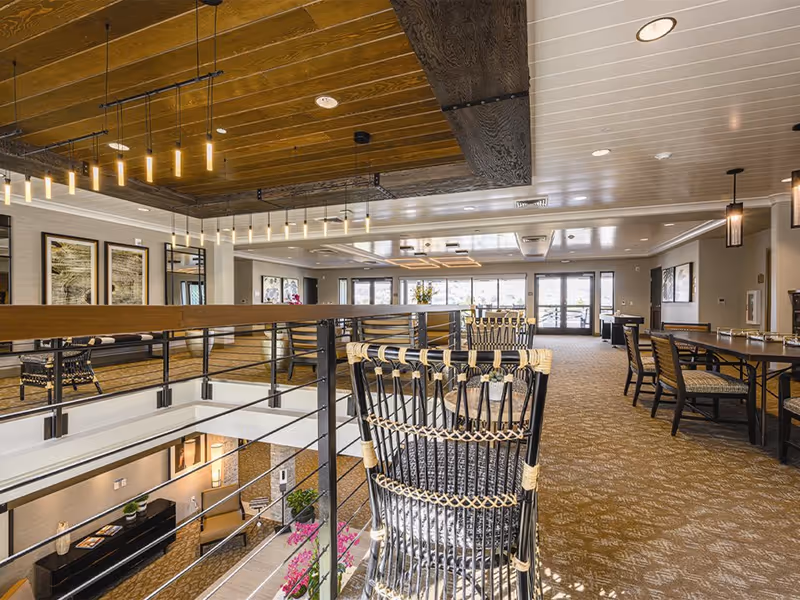 Spacious, well-lit communal dining and lounge area with wicker chairs, tables, and an interior balcony overlooking the lobby.