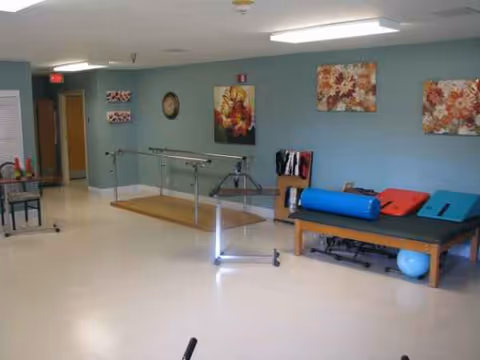 Rehabilitation therapy room with parallel bars, mats, and exercise equipment along a blue wall.