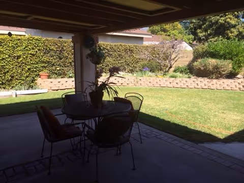 Patio area at Pilarville Garden with a table, chairs, and lawn beyond.