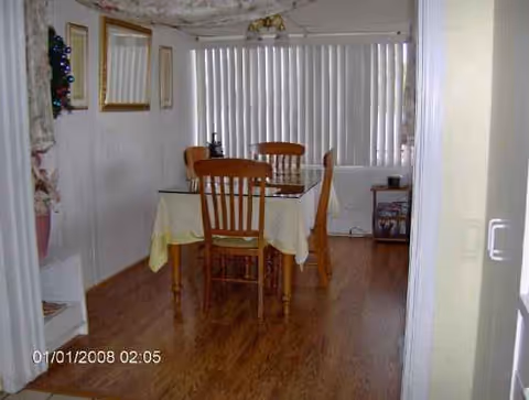 A small dining room with a wooden table, four chairs, and yellow tablecloth under vertical blinds.