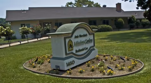 Front exterior view of Mission Gardens Assisted Living with a landscaped sign and lawn.