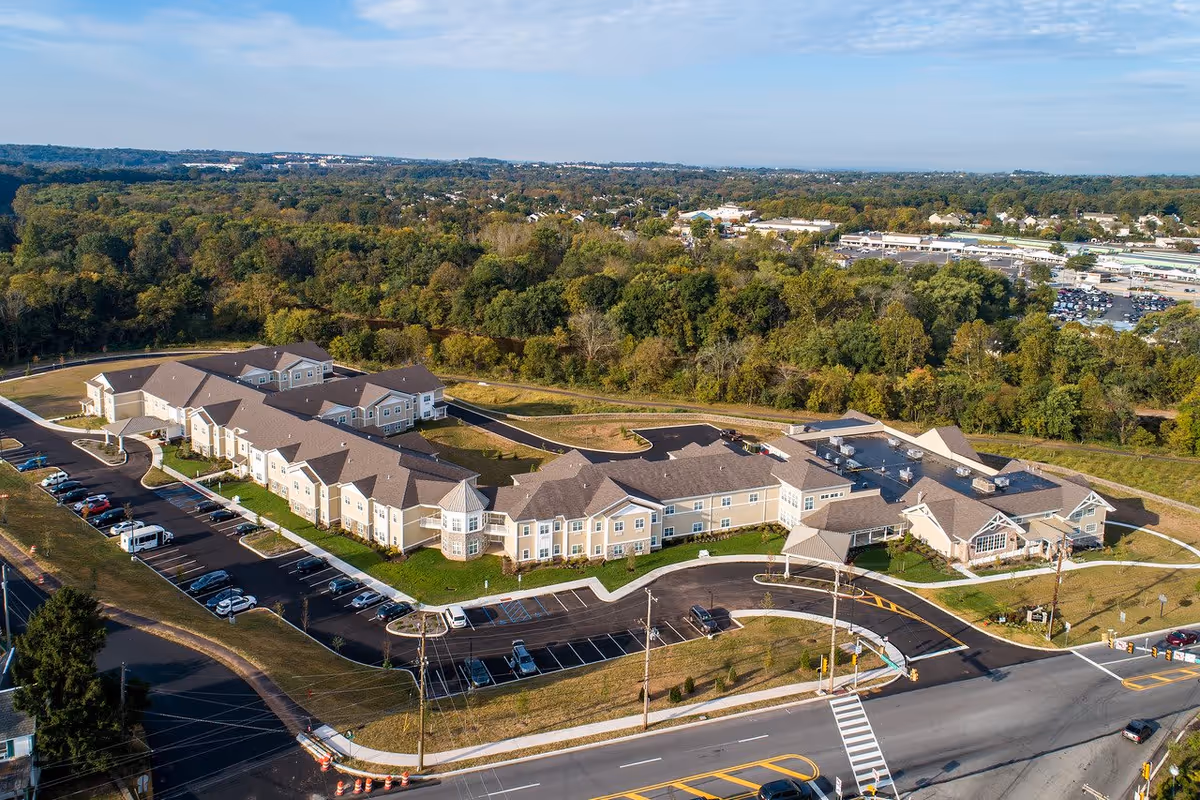 Aerial view of a large senior living complex with connected beige buildings, parking lots, and surrounding trees.