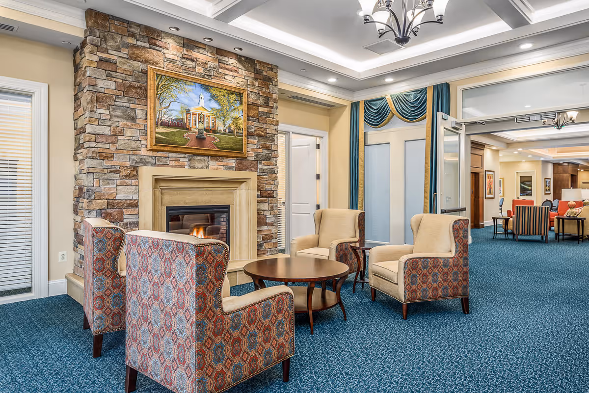 Cozy lounge with four upholstered armchairs around a round coffee table in front of a stone fireplace and painting.
