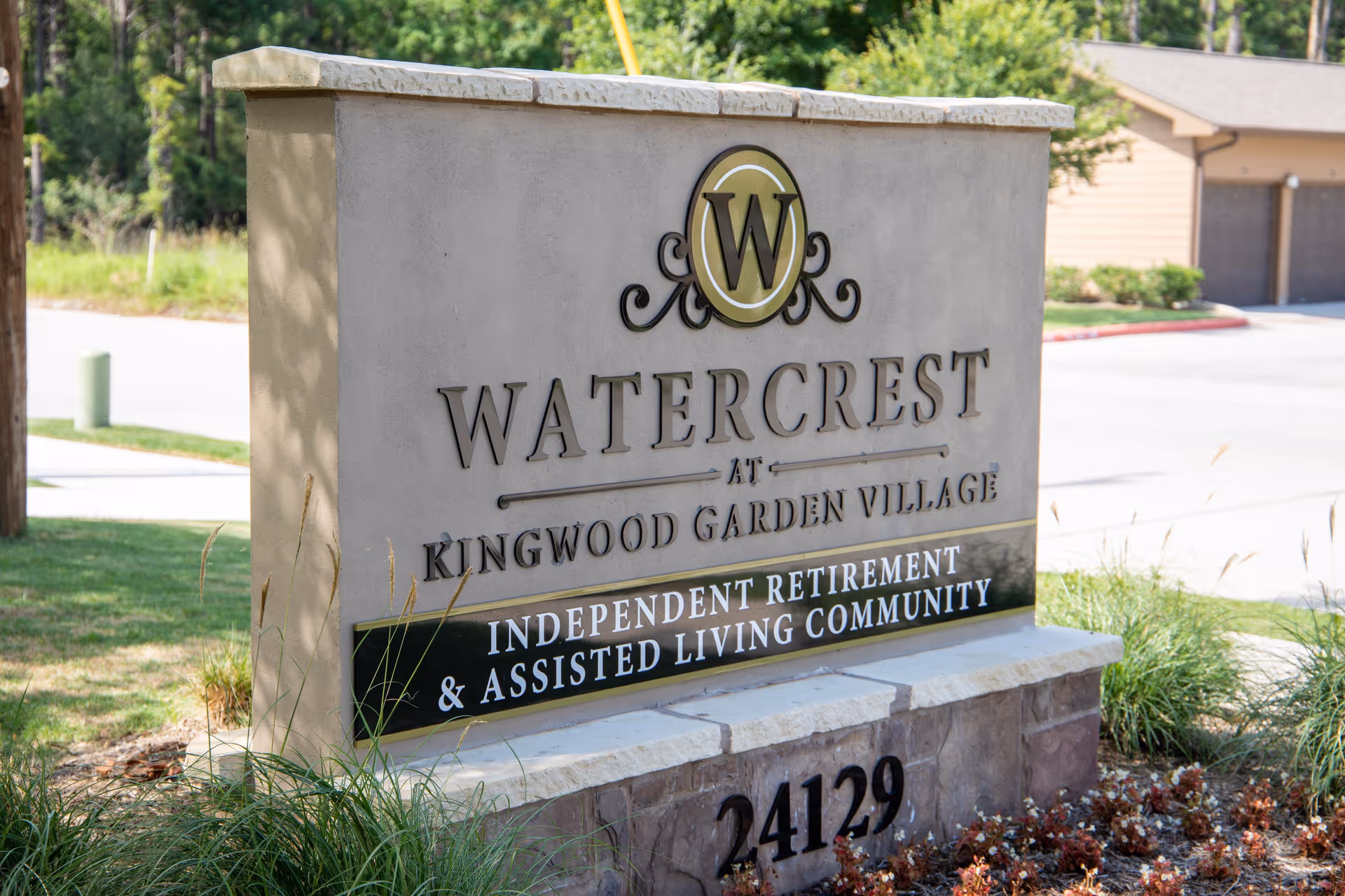 Stone sign for Watercrest at Kingwood Garden Village, an independent retirement and assisted living community, with landscaping and a driveway in the background.