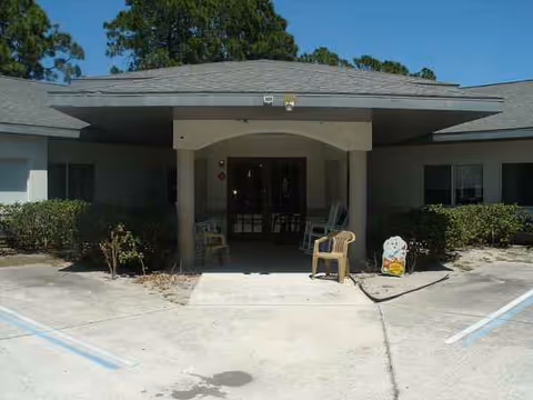 Entrance to a senior living facility with a covered drop-off area and chairs.