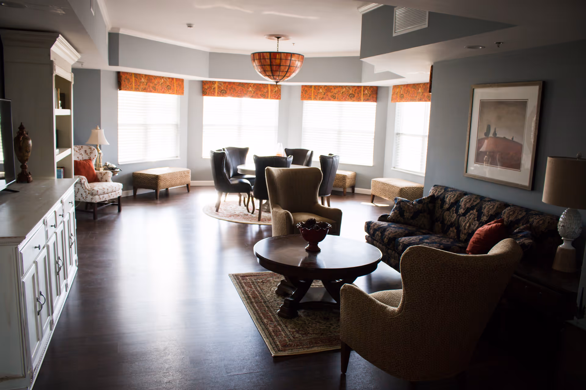 Common living room with sofas, armchairs, a round coffee table and a bay of bright windows.
