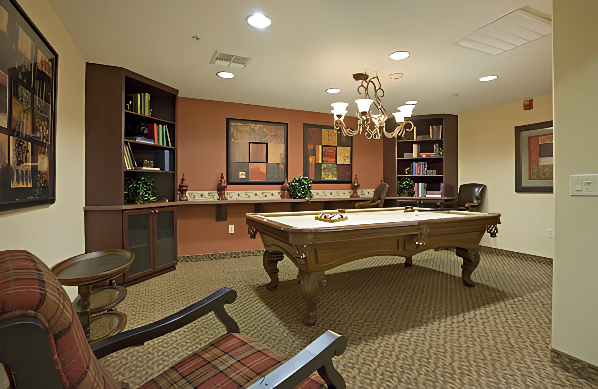 Well-lit interior game room with a pool table, seating, bookshelves and wall art.