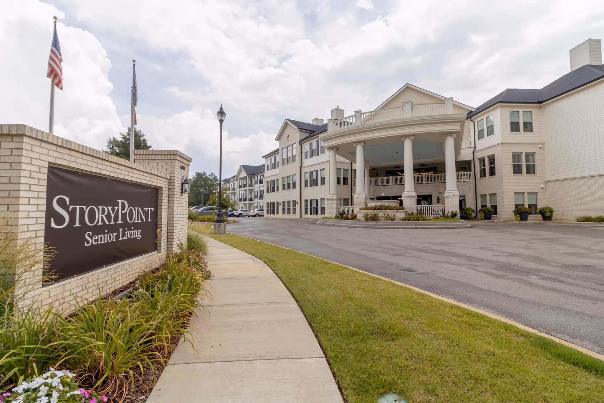 The front entrance and driveway of a multi-story StoryPoint Senior Living building with a brick sign, columns, and a sidewalk.