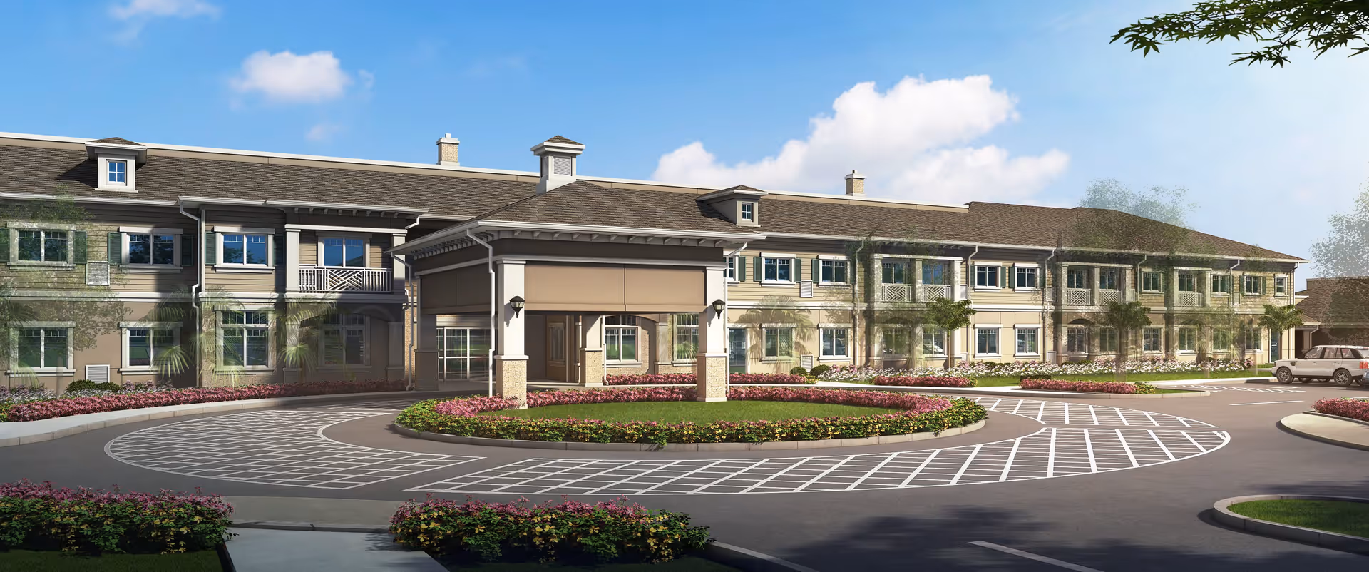 Exterior view of a large two-story senior living facility building with a covered entrance, surrounded by landscaped flower beds and a circular driveway under a blue sky with some clouds.