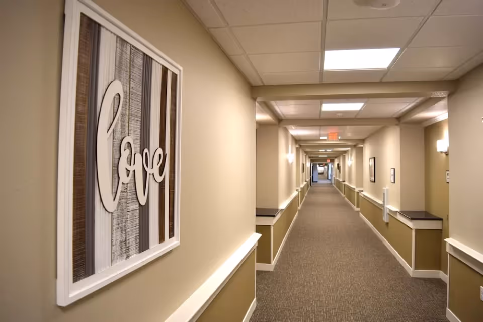 Long, well-lit interior hallway with beige walls and a framed 'Love' sign on the left.
