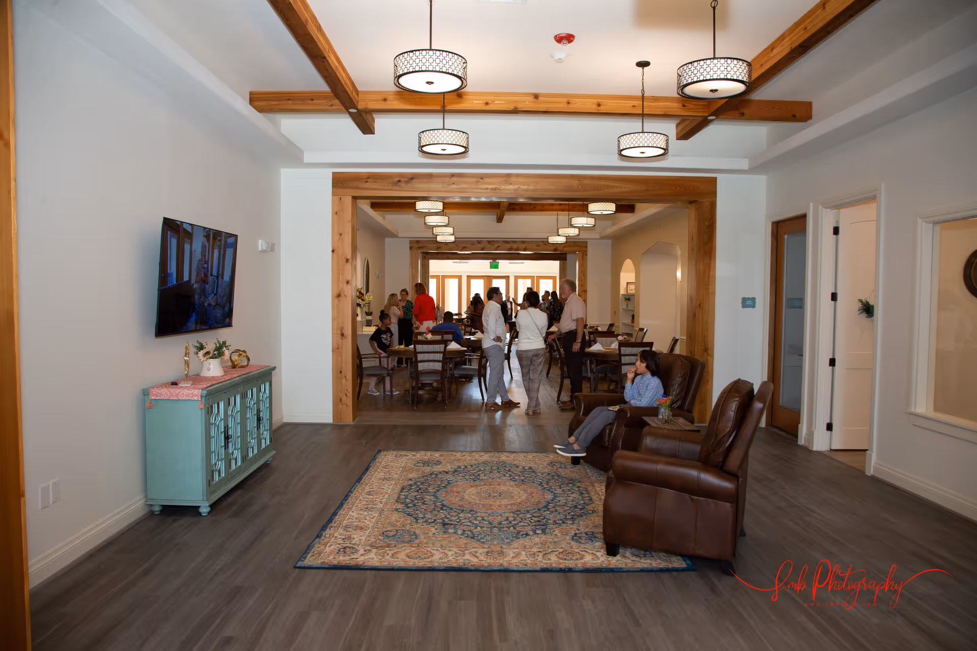Open common area with recliner seating, a TV, rug, and people gathered around tables in the background.