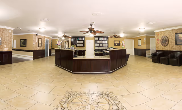 Spacious interior lobby with a central wooden reception desk, tiled floor, ceiling fans, and seating areas.