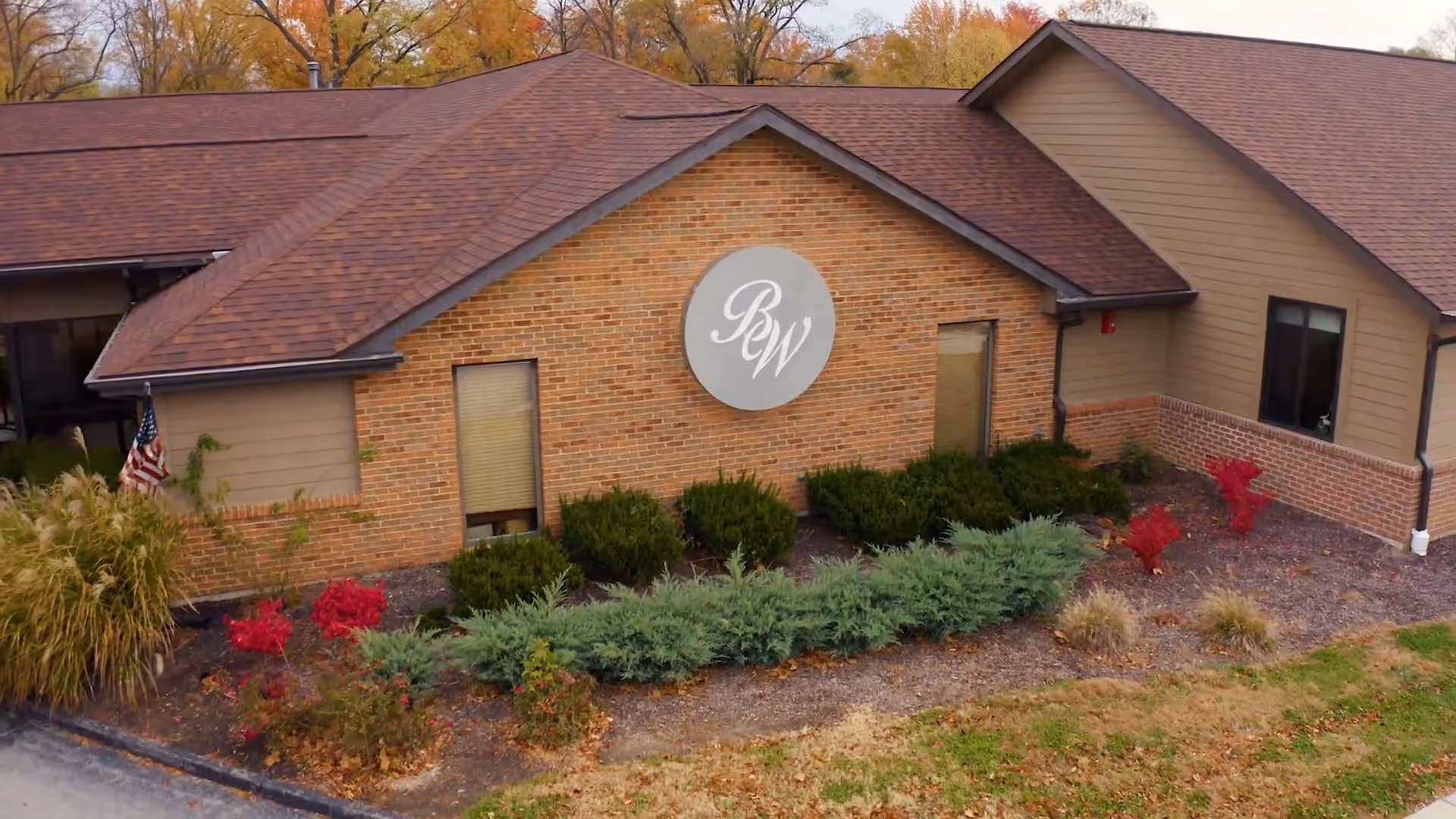 Front exterior of a single-story brick building with a circular 'BW' logo above landscaped shrubs.