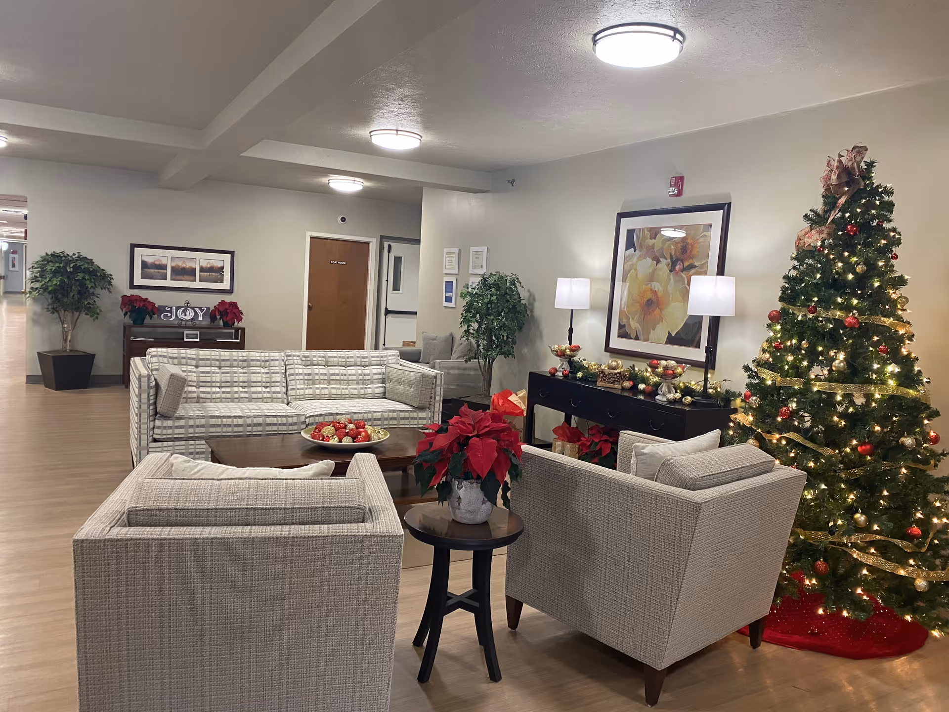 Seating lounge with sofas and armchairs arranged around tables, holiday poinsettias and a decorated, lit Christmas tree.