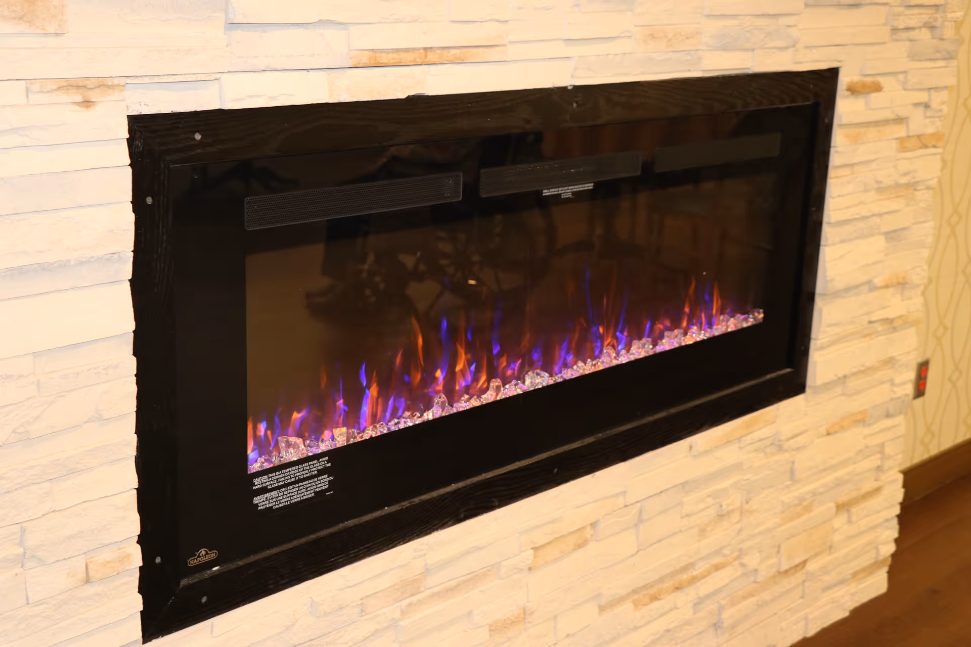 Modern electric fireplace with purple-blue flames set in a stone-clad interior wall.