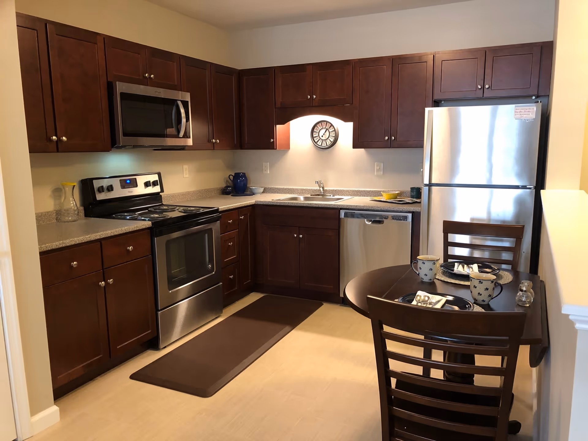 Modern kitchen with dark wood cabinets, stainless steel appliances, and a small dining table set for two.