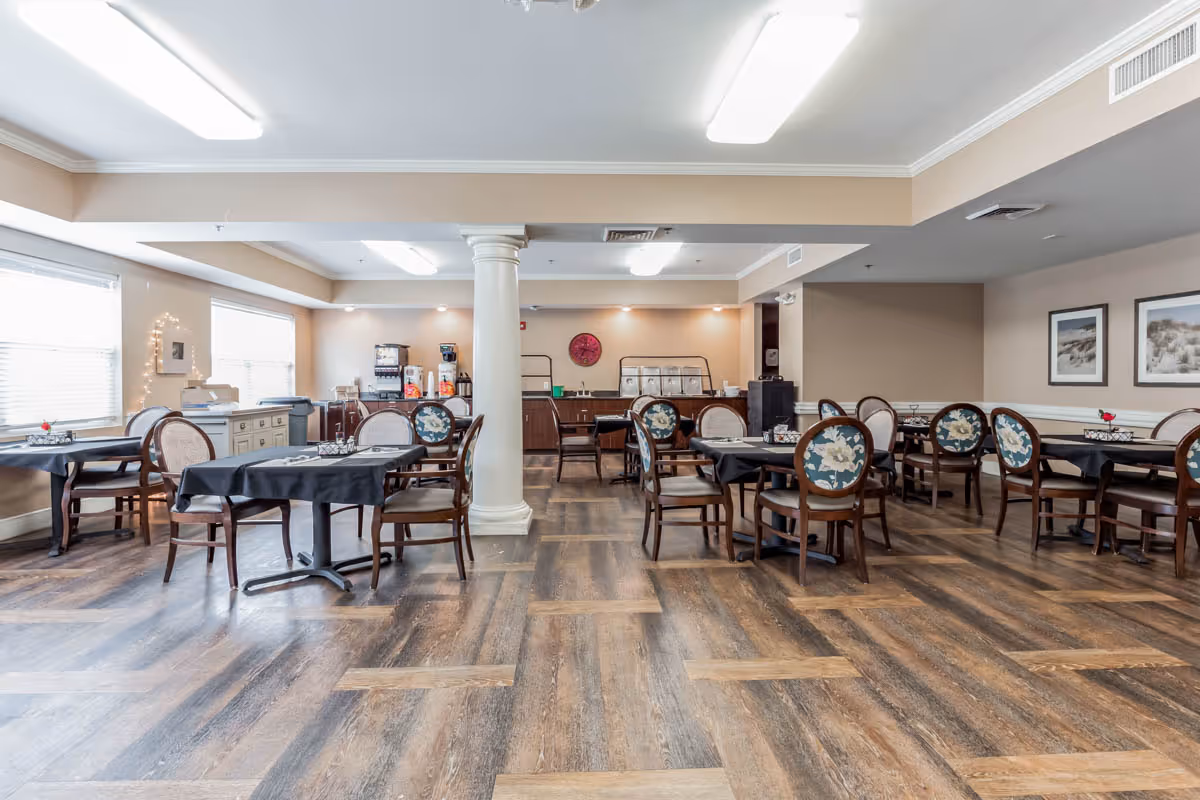 Spacious dining room with multiple tables and upholstered chairs, a central column, buffet/coffee station, and wood flooring.