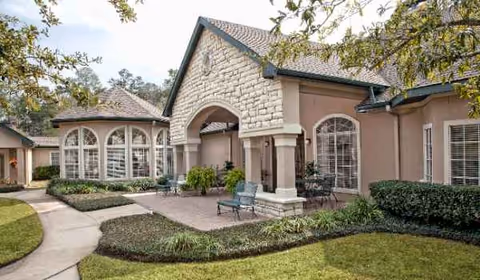 Stone-clad senior living facility exterior with arched windows, columns, and landscaped courtyard.