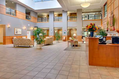 Spacious two-story atrium lobby with seating areas, a reception desk, potted plants, and a skylight.