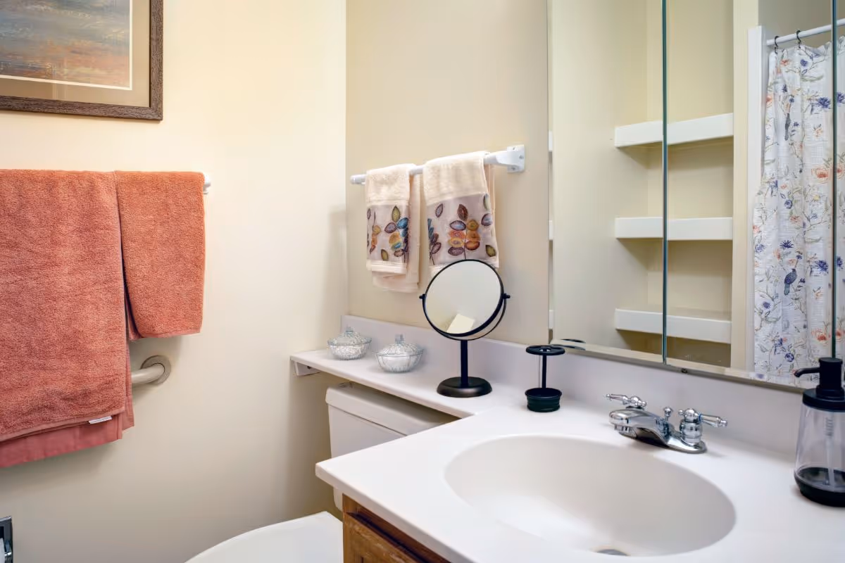 A clean bathroom featuring a sink and vanity with a mirror, folded towels, and a floral shower curtain.