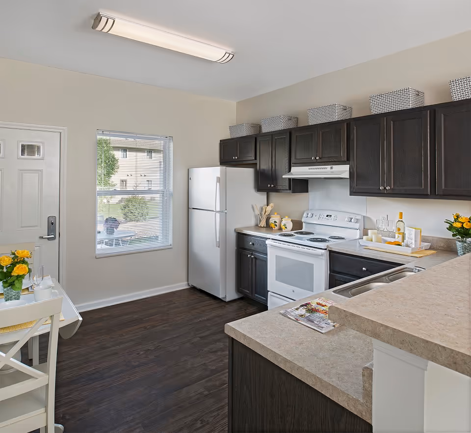 Bright modern kitchen with dark cabinets, white appliances, a small dining table, and a window.