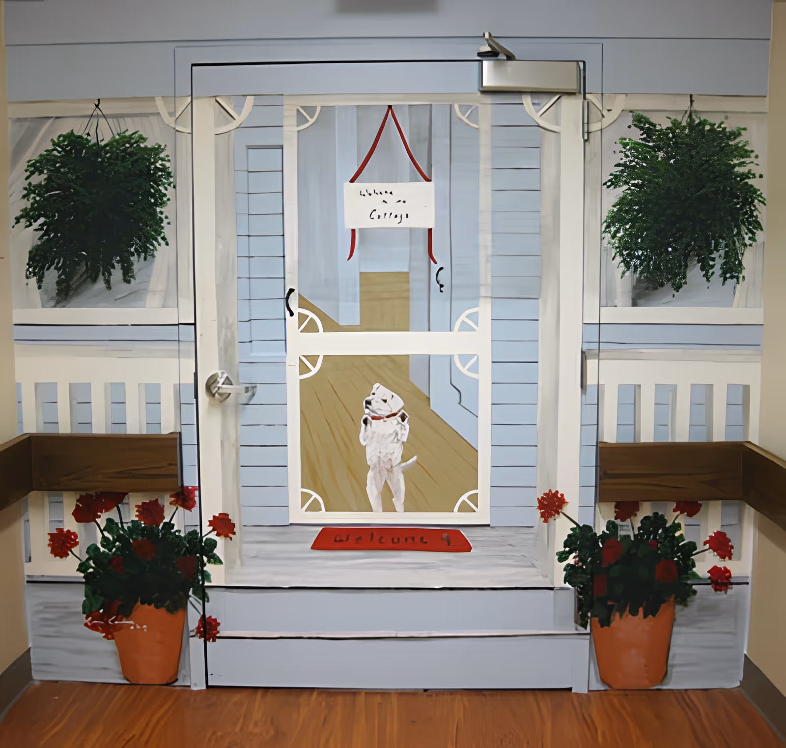 A painted mural on a wall depicting a porch scene with a screen door, two hanging green plants, two flower pots with red flowers, and a small white dog standing on its hind legs behind the door. The door has a sign hanging that reads 'Welcome Cottage'.