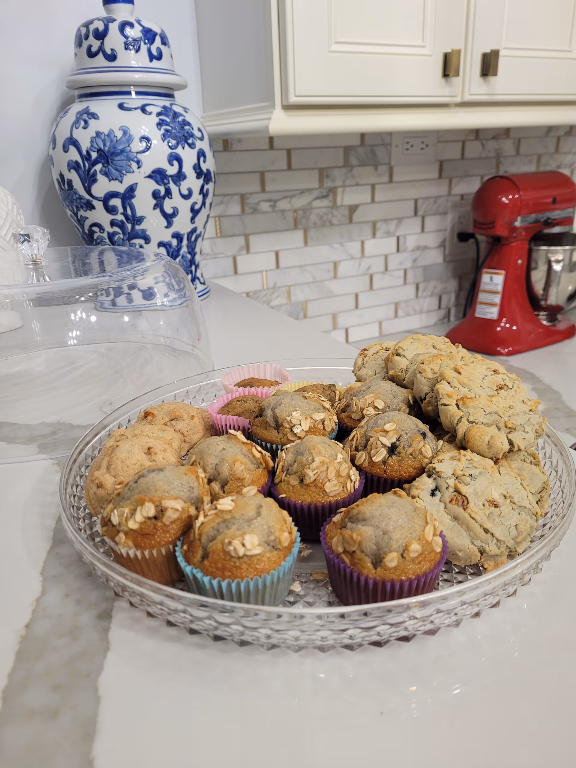 Tray of muffins and scones on a kitchen counter with a blue-and-white vase and a red stand mixer in the background.