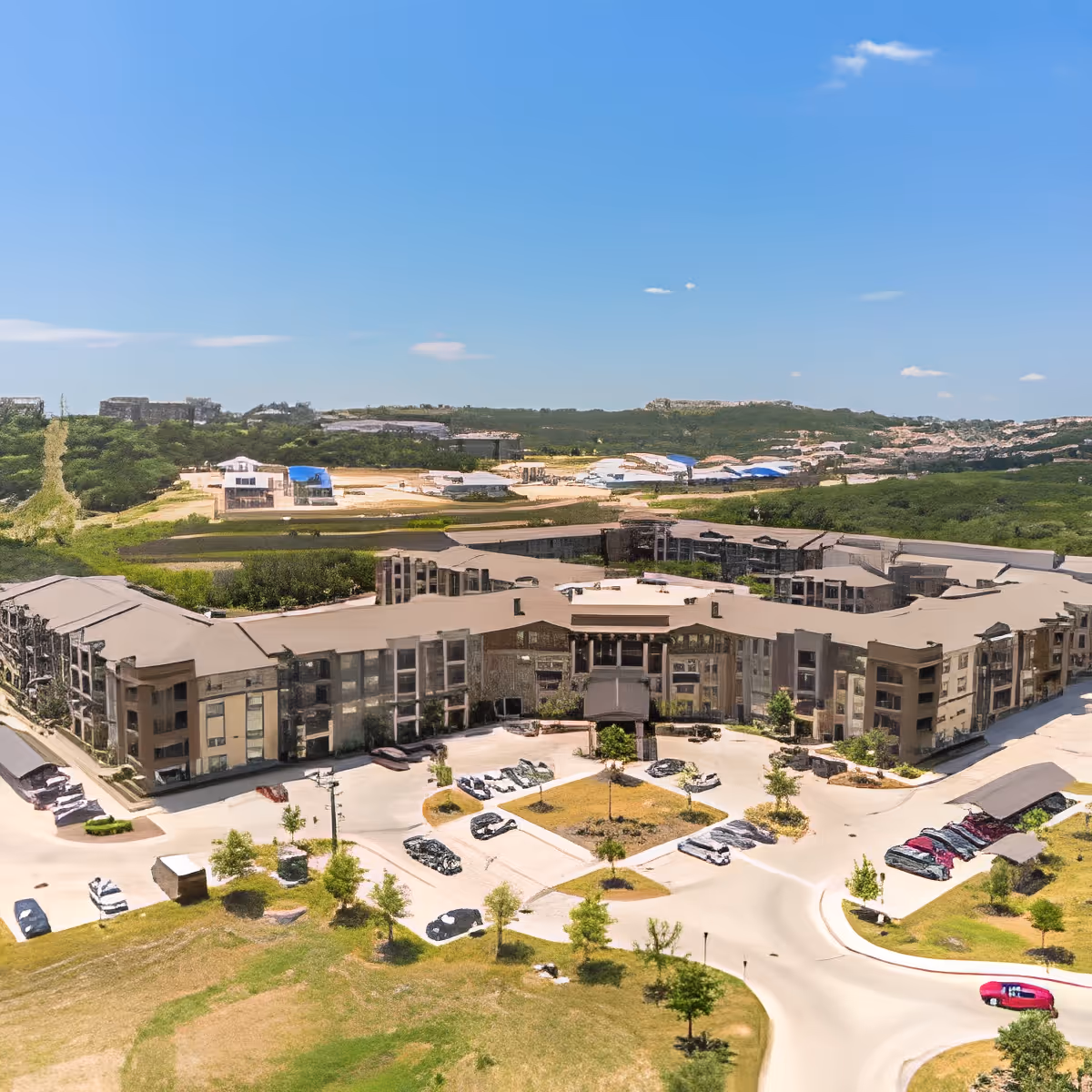 Aerial view of Discovery Village At Dominion, a large senior living facility surrounded by greenery and parking areas under a clear blue sky.