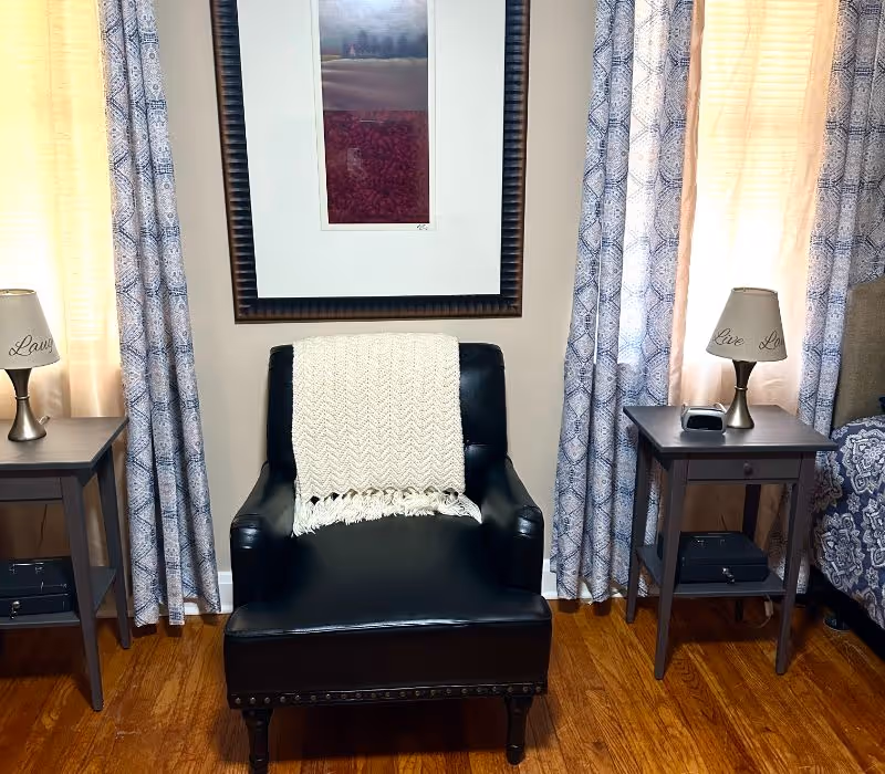 Cozy bedroom seating area with black leather chair, two end tables, lamps, and framed art.