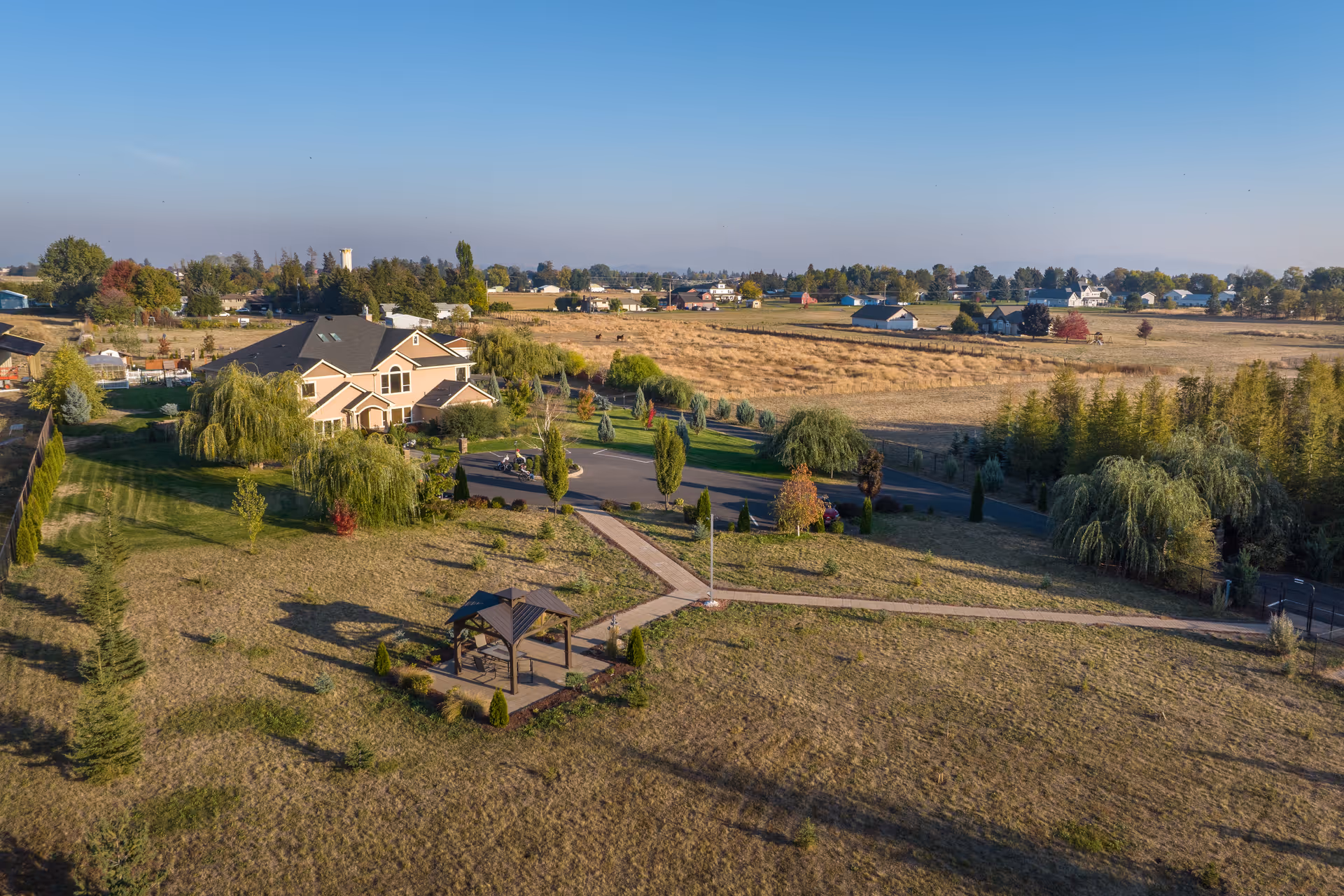 Aerial view of a large country home with landscaped grounds, a gazebo, walking paths and surrounding fields.