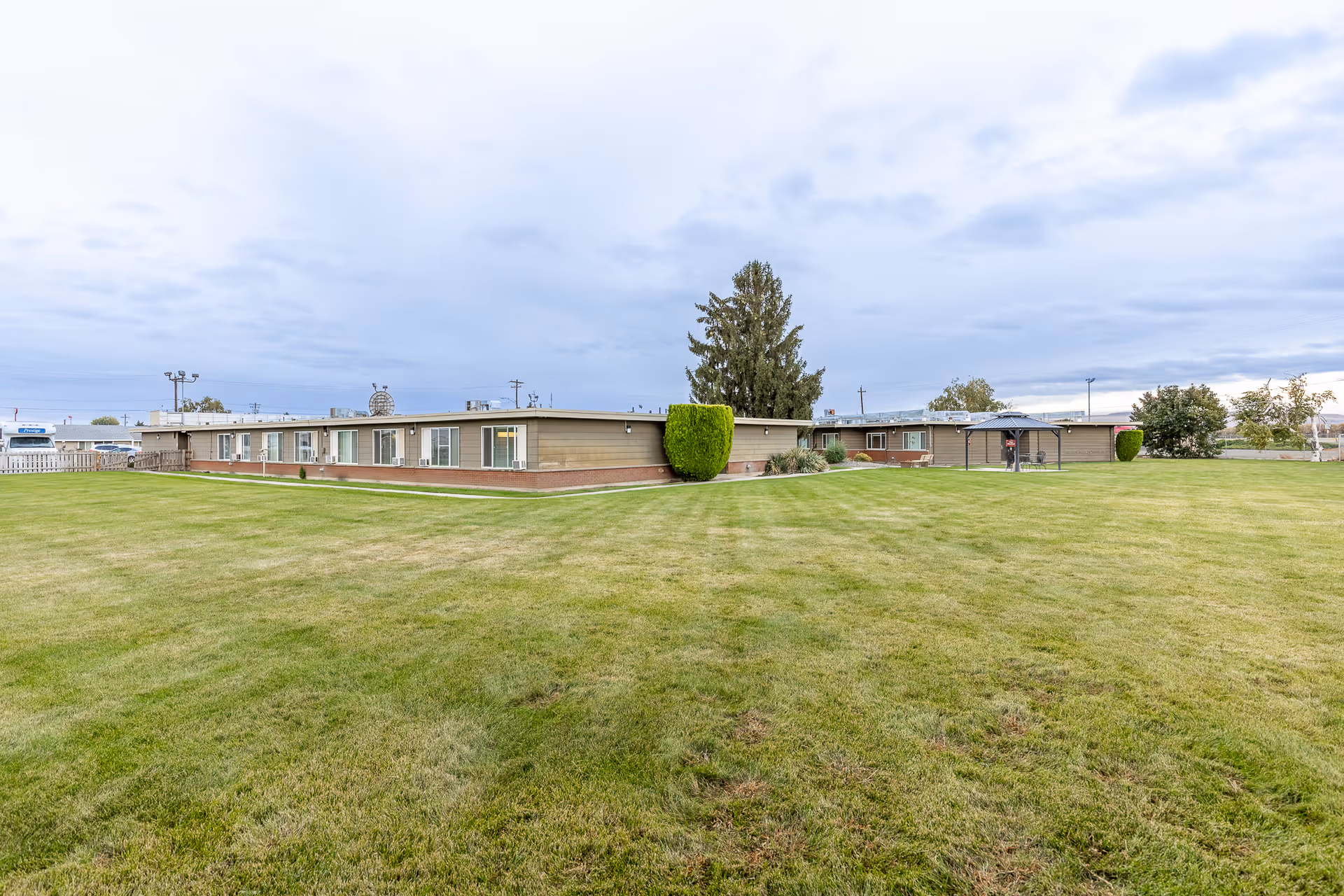 Single-story facility building set behind a large manicured lawn under a cloudy sky.