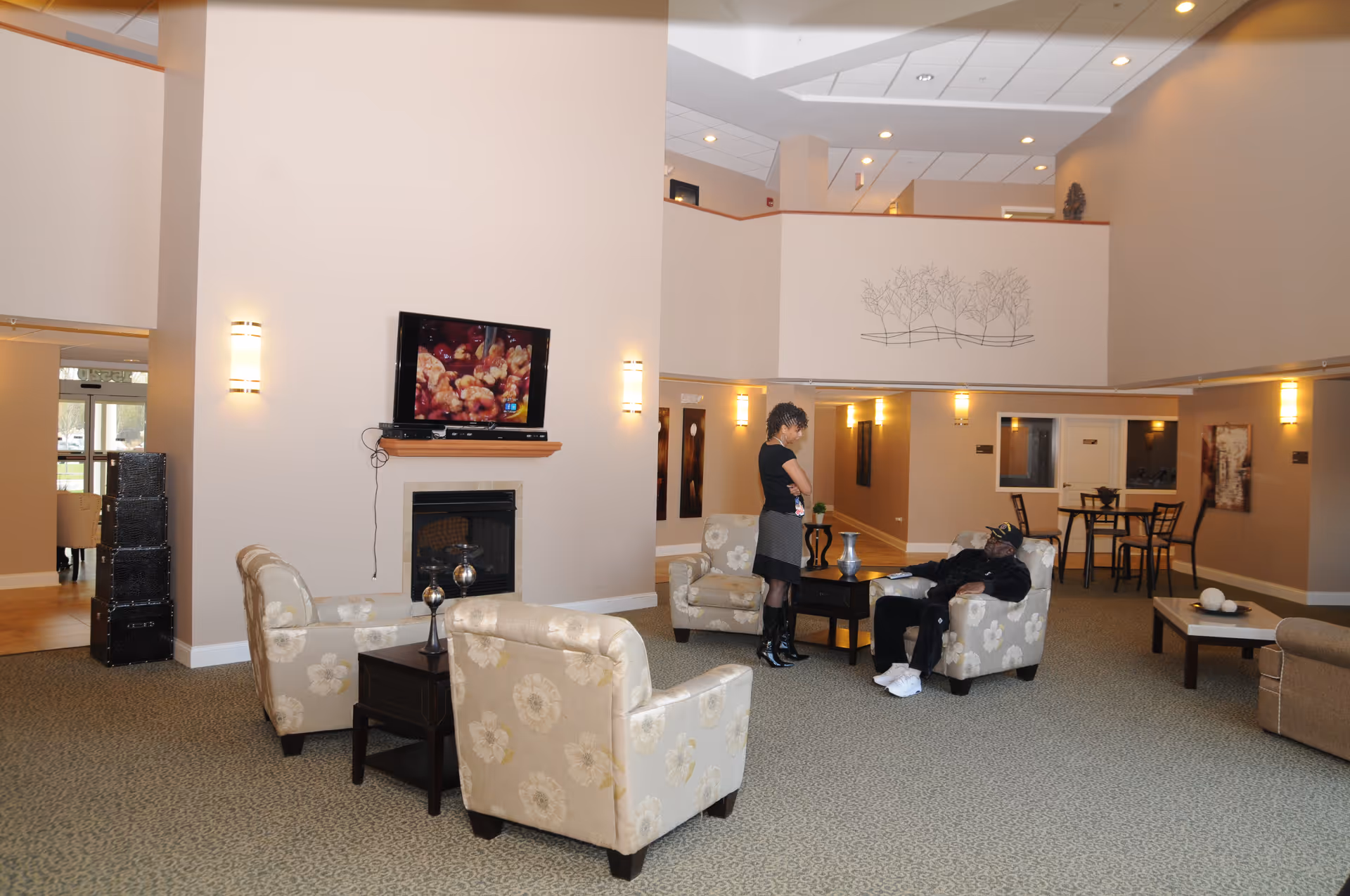 Spacious senior living lounge with sofas, fireplace, TV, and residents chatting nearby