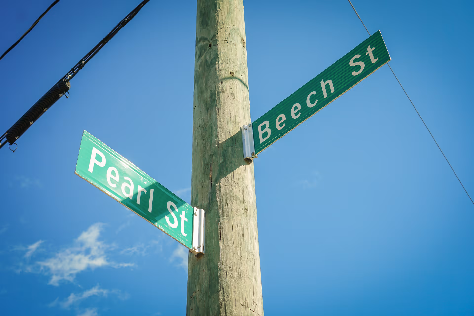 Green street signs reading 'Pearl St' and 'Beech St' mounted on a wooden utility pole against a clear blue sky.