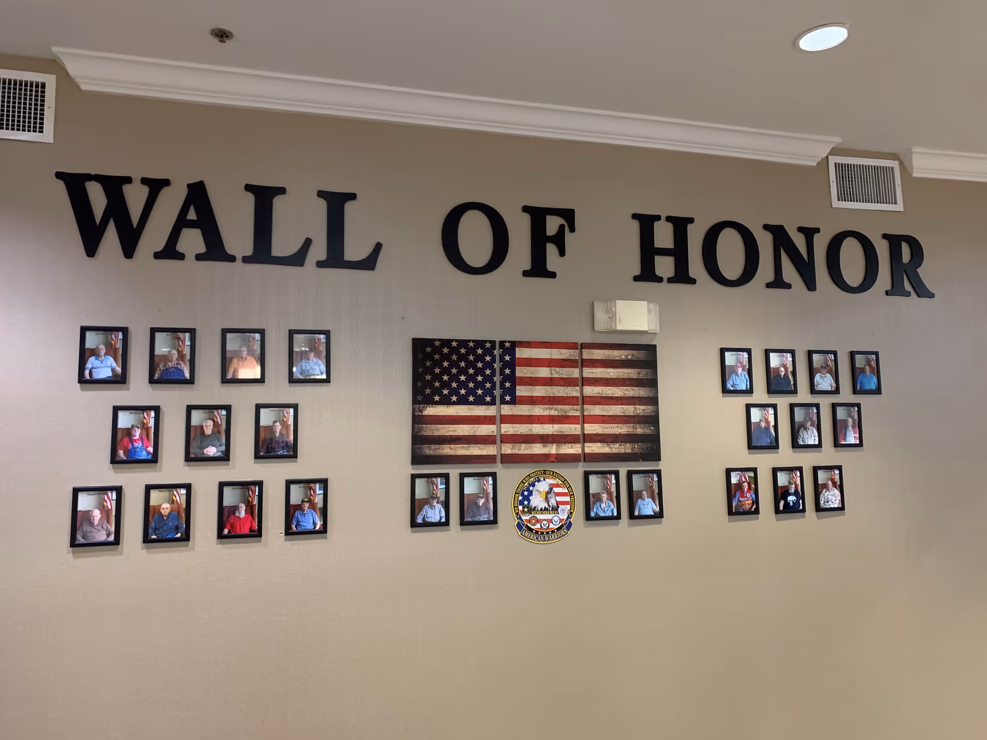 Interior wall display reading 'WALL OF HONOR' with an American flag and multiple framed photos of residents.