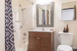 Bathroom with a shower-tub and patterned curtain, a wooden vanity with mirror, and a toilet.