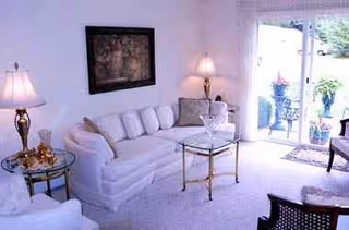 Bright white living room with a white sofa, glass coffee table, and lamps.