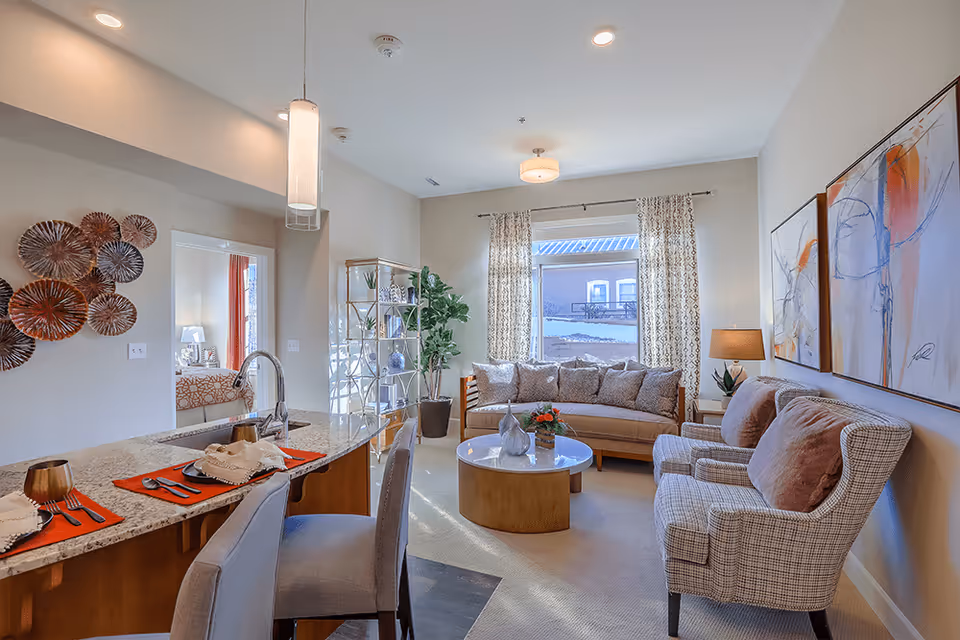 Bright open living room with a sofa, armchairs, coffee table, and a kitchen island with place settings.