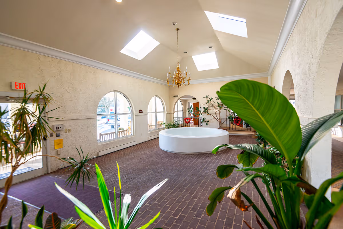 Atrium-style lobby with skylights, a central round planter/fountain, chandelier, arched windows and indoor plants.