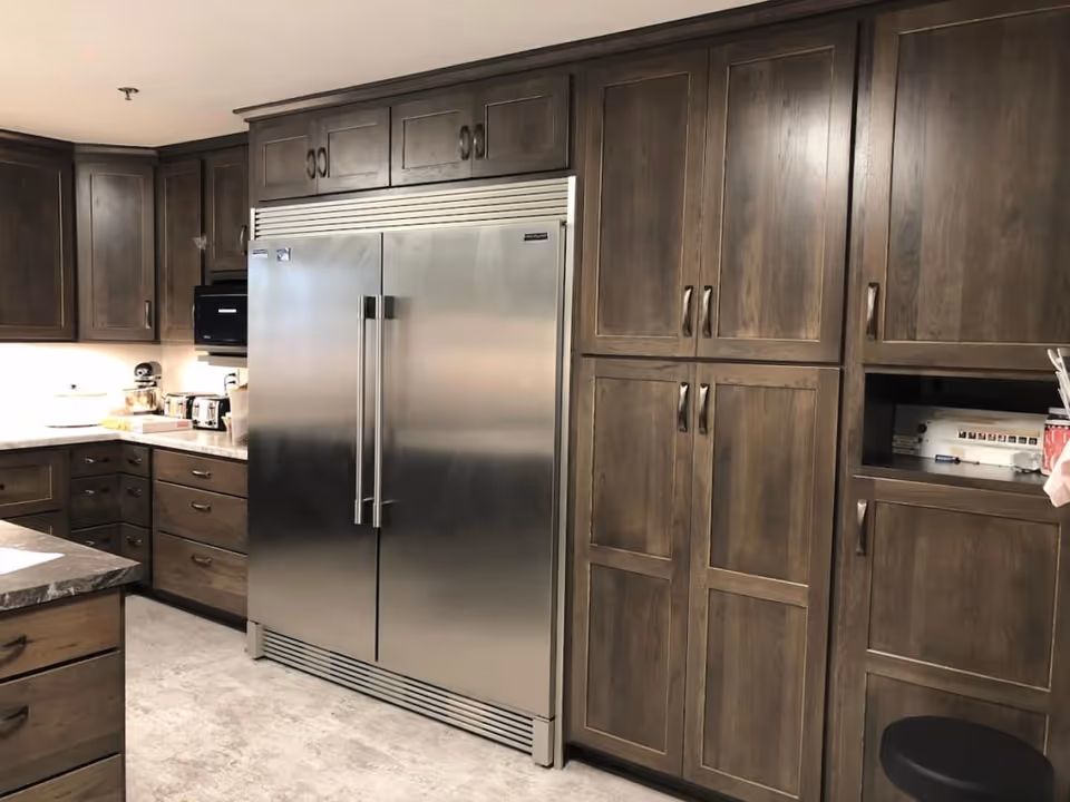 Kitchen interior with a large stainless-steel double-door refrigerator built into dark wood cabinetry and surrounding drawers and counters.