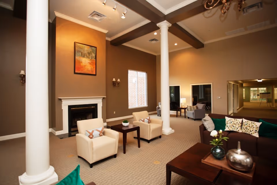 Spacious lounge with armchairs, sofas, coffee tables, a fireplace and decorative columns under warm lighting.