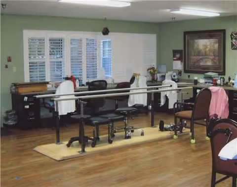 Rehabilitation therapy room with parallel bars, chairs, and desks in Cedarcrest Manor.